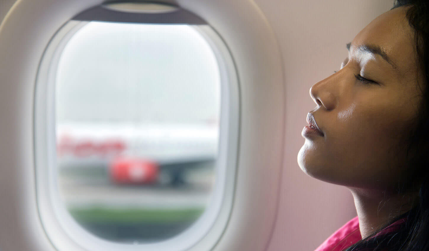 junge Asiatin sitzt mit geschlossenen Augen im Flugzeug